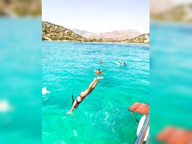 A group of friends enjoys a refreshing swim in crystal-clear turquoise waters, with one diving in for a splash — perfect for summer adventures on the water.