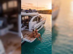 Two women enjoy a sunset on the edge of a luxurious yacht, dipping their feet in the clear waters — a perfect moment for relaxation and celebration on the water.