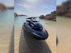 A sleek black jet ski rests on the sandy shore, surrounded by clear waters and rocky landscapes, perfect for thrilling water adventures.