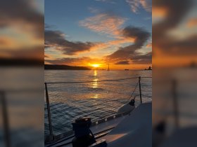 A stunning sunset view from the deck of a sailboat, showcasing the tranquil waters and distant silhouettes of other vessels — perfect for romantic evening cruises.