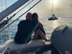 A couple enjoys a romantic moment on the deck of a yacht, overlooking a serene sunset on the water — perfect for intimate getaways.