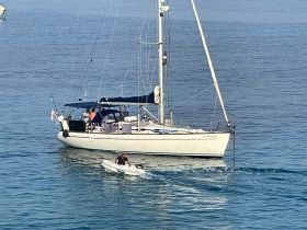 A sailboat navigates the serene waters while a small dinghy approaches, showcasing a perfect day on the water.