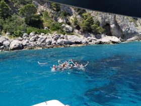 A lively group enjoys a refreshing swim in crystal-clear waters, surrounded by stunning coastal scenery — perfect for summer adventures.
