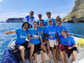 A lively group of friends enjoys a day on the water, celebrating together on a boat with stunning coastal views in the background.
