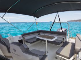 A spacious and stylish interior of a Jeanneau boat, featuring comfortable seating and a table, perfect for relaxing while enjoying the stunning turquoise waters.