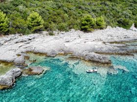 Aerial view of a couple enjoying a serene moment on a small boat amidst crystal-clear waters and rocky coastline, perfect for exploring hidden gems in nature.