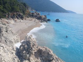 A stunning view of a secluded beach with crystal-clear waters, featuring a person swimming in the distance — an ideal spot for relaxation and exploration.