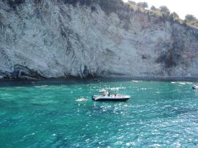 A vibrant scene featuring a boat with guests enjoying the clear turquoise waters, surrounded by stunning coastal cliffs — perfect for a day of adventure and relaxation.