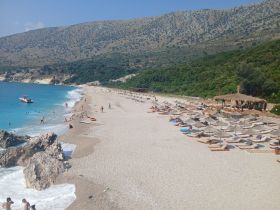 A vibrant beach scene with people enjoying the sun and swimming in the turquoise waters, complemented by a boat anchored nearby — perfect for a day of relaxation and fun by the sea.