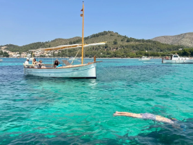 A group enjoys a sunny day on a boat while one person swims in the crystal-clear waters, showcasing the perfect summer getaway.