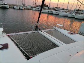 A serene view of a catamaran docked at sunset, showcasing its spacious netting and tranquil waters — perfect for relaxing sailing adventures.