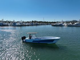 A sleek speedboat is docked in a marina, showcasing its vibrant design against a backdrop of luxury yachts — perfect for day trips or fishing adventures.