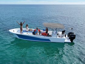 A lively group enjoys a fun day on the water, with one person celebrating on the bow of the boat while others relax and swim nearby.