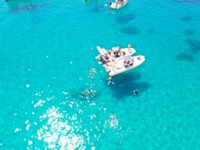 A vibrant scene of a group enjoying snorkeling and swimming in crystal-clear turquoise waters, with boats anchored nearby — a perfect day for aquatic adventures.