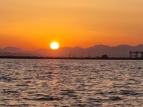 A stunning sunset over the water, with mountains in the background, creating a picturesque scene perfect for evening boat cruises.