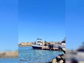A fishing boat is docked with crew members preparing for a day on the water, showcasing the vibrant marina setting under a clear blue sky.