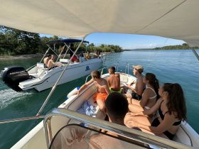 A lively group of friends enjoys a sunny day on the water, engaging with another boat while soaking up the summer vibes.