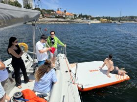 A lively group enjoys a sunny day on the water, with friends gathered on a boat and a floating mat, perfect for summer fun and relaxation.