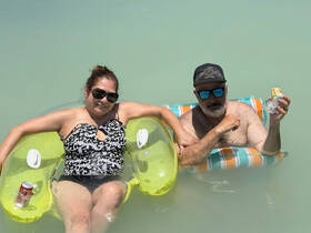 A couple enjoys a relaxing day in the water, lounging on inflatable floats while sipping drinks and savoring snacks — a perfect beach getaway.