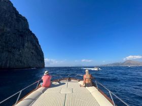 A couple enjoys a scenic boat ride along a stunning coastline, with dramatic cliffs and clear blue waters creating the perfect backdrop for a memorable day on the ocean.