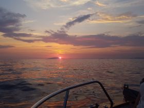 A serene sunset view from a boat, showcasing the vibrant colors reflecting on the water — perfect for romantic evening cruises.