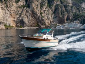 A sleek speedboat navigates the shimmering waters near a stunning coastline, showcasing the beauty of the surrounding cliffs and seaside village.