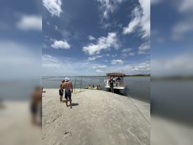 A lively group enjoys a sandbar stop with a boat anchored nearby, perfect for swimming and socializing under the sun.