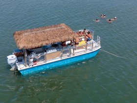A lively group enjoys a day on a pontoon boat, with some swimming in the water and others relaxing on deck — perfect for a fun-filled outing.