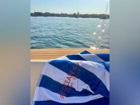 A striped towel featuring 'Ocean 45 Boat Tours' rests on the edge of a boat, with a serene waterfront view in the background, perfect for a day of relaxation on the water.