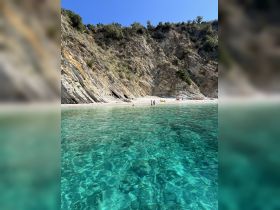 A picturesque beach scene featuring a couple enjoying the clear turquoise waters, framed by stunning rocky cliffs — an ideal spot for relaxation and exploration.