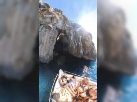 A lively group enjoys a sunny day on a boat near a stunning cave, perfect for swimming and exploration — an ideal setting for memorable adventures on the water.