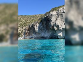 A stunning view of a rocky coastline with crystal-clear waters, showcasing a beach area where guests enjoy the sun and surf — perfect for a day of relaxation and exploration.
