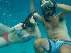 A couple enjoys snorkeling underwater, giving thumbs up in a vibrant marine setting — a perfect snapshot of adventure and fun in the water.