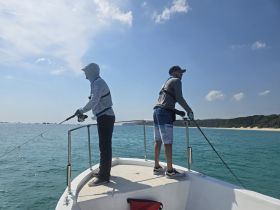 Two friends enjoy a fishing trip on a boat, casting their lines into the clear blue ocean — a perfect day for outdoor adventure.