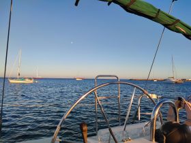 A serene view of multiple sailboats anchored in calm waters during sunset, showcasing the beauty of a peaceful marina setting.