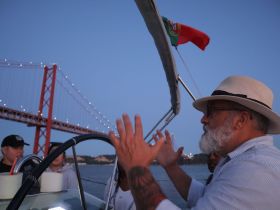 A group enjoys a scenic boat ride in Lisbon, with a stunning view of the illuminated bridge at dusk. The atmosphere is lively as they engage in conversation, making it a perfect backdrop for memorable experiences on the water.