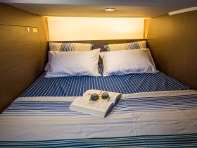 Cozy cabin interior featuring a neatly made bed with striped linens, perfect for relaxation on a boat getaway.