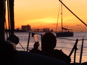A silhouette of a person toasting with a glass against a stunning sunset backdrop, capturing the essence of a serene sailing experience.