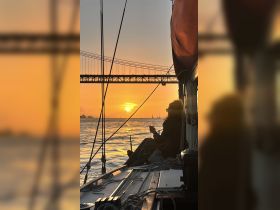 A serene sunset view from a sailboat, featuring a guest enjoying a drink while taking in the beautiful scenery — perfect for romantic evenings on the water.