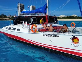 A lively group enjoys a day on the Pura Vida catamaran, soaking up the sun and relaxing on the deck in beautiful turquoise waters.