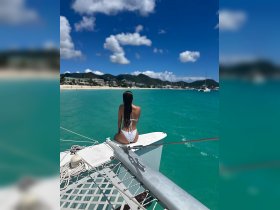 A woman enjoys the stunning view from the bow of a catamaran, overlooking a beautiful beach and turquoise waters — a perfect moment for relaxation and adventure.
