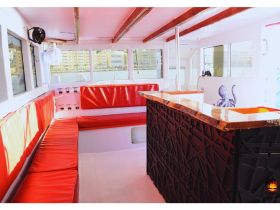 Interior view of a stylish boat cabin featuring comfortable red seating and a sleek bar area, perfect for relaxing while enjoying the water.