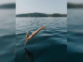 A woman dives gracefully into the crystal-clear ocean, capturing the thrill of summer adventures and water activities near a picturesque island backdrop.