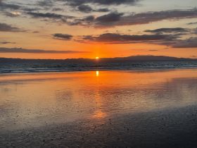 A serene sunset over the ocean, reflecting vibrant colors on the water's surface, creating a picturesque coastal scene.