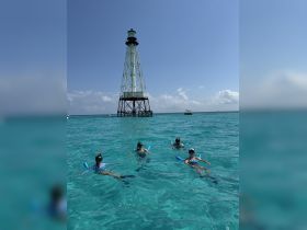 A group of snorkelers enjoys a sunny day in crystal-clear waters near a lighthouse, making for an unforgettable aquatic adventure.