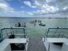 A lively group enjoys a fun day in the water, engaging in swimming and relaxation while surrounded by boats — perfect for a memorable day out on the water.