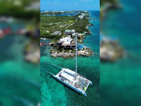 An aerial view of a lively catamaran cruising through clear turquoise waters, with guests enjoying the sun and scenery — perfect for group outings and island adventures.