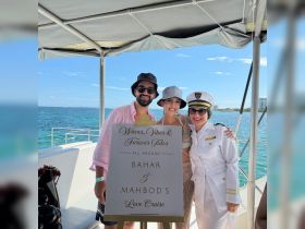 A joyful couple celebrates their love aboard a cruise, posing with a personalized sign on a beautiful day at sea — perfect for romantic getaways and special occasions.