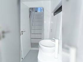 A clean and modern interior view of a boat's bathroom, featuring a sleek sink and stairs leading to the upper deck.