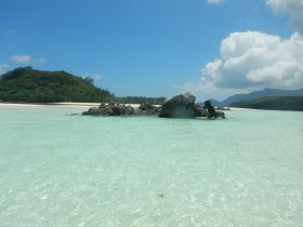 A stunning view of a secluded beach with crystal-clear waters and rocky formations, perfect for a tranquil getaway or island exploration.